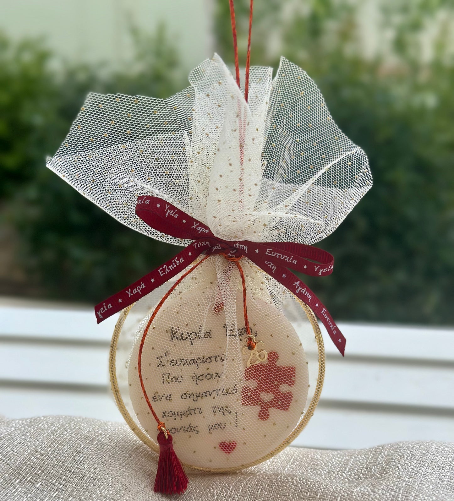 Χειροποίητο γούρι δασκάλας μέσα σε λευκό τούλι με χρυσές κουκκίδες, διακοσμημένο με μπορντό κορδέλα, χρυσό περίγραμμα και κόκκινο φούντι.