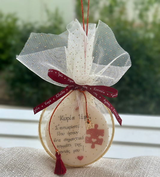 Χειροποίητο γούρι δασκάλας μέσα σε λευκό τούλι με χρυσές κουκκίδες, διακοσμημένο με μπορντό κορδέλα, χρυσό περίγραμμα και κόκκινο φούντι.